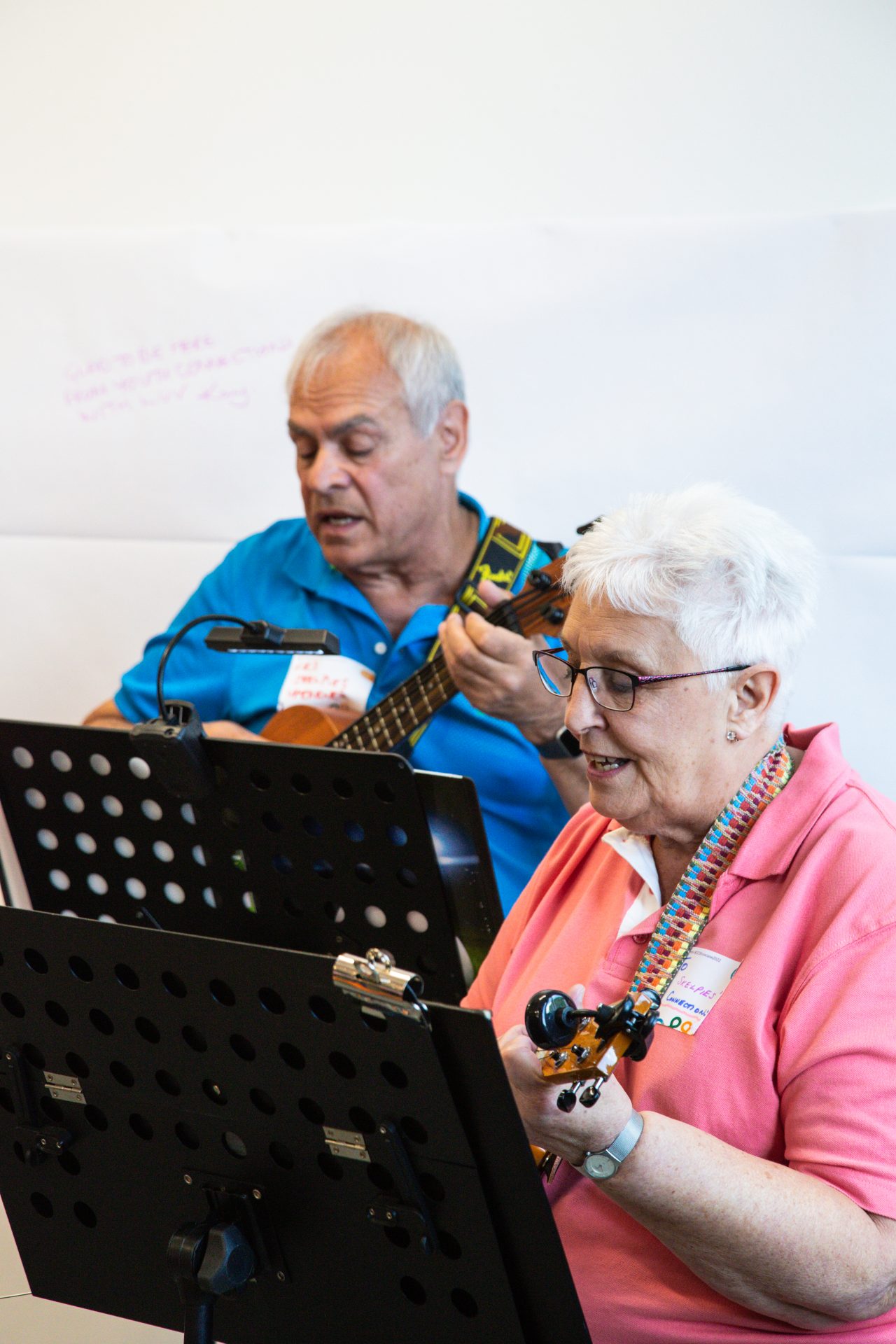 man and woman playing ukulele behind music stands.